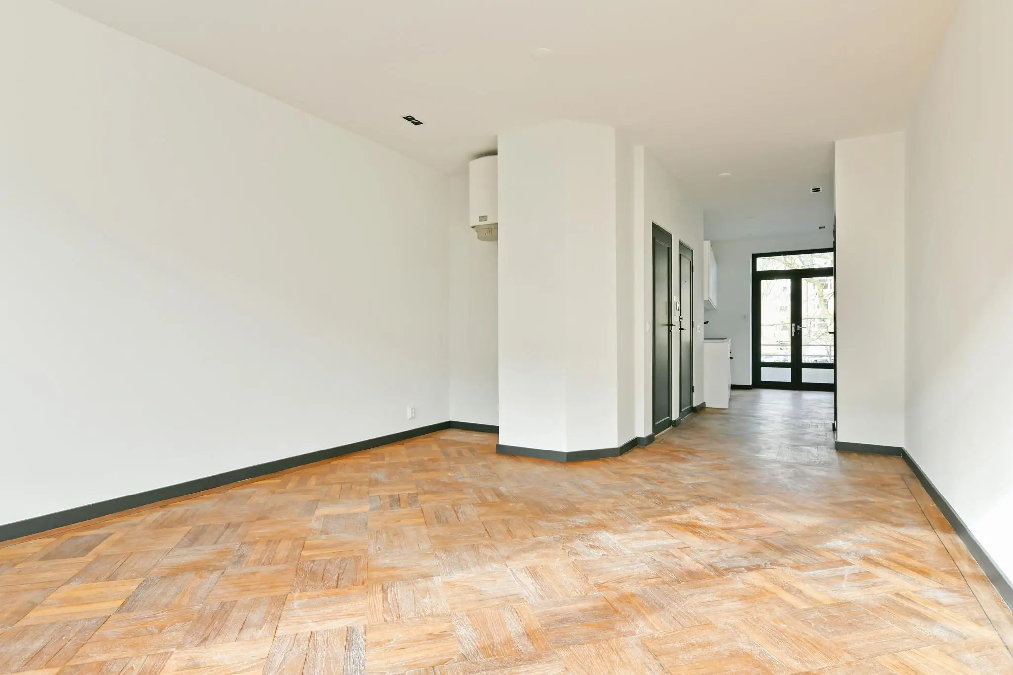 Lichte, lege woonkamer met houten visgraatvloer aan de Cornelis Dopperkade.